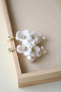 Macro shot of white ceramic flower earrings with pearl accents and gold metal finish