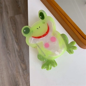 Makroaufnahme einer süßen grünen Frosch-Haarklammer mit cremefarbenen Wolkenmustern