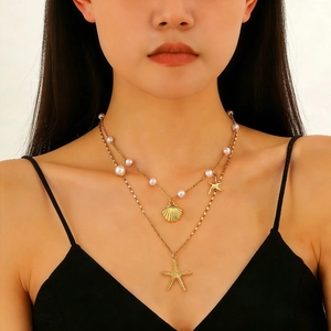 Dettaglio di una collana a strati dorata con conchiglia, stella marina e perle