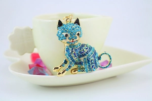 Close-up of golden lucky cat pendant with blue rhinestones and enamel on white ceramic cup