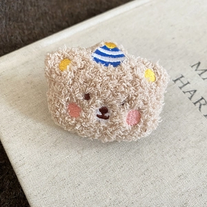 Macro view of a cute khaki flocked bear brooch with soft plush texture and embroidery