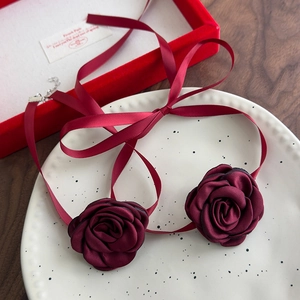 Burgundy satin rose choker necklace with long ribbon ties on a decorative ceramic plate