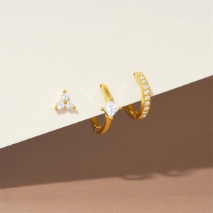 Close-up of a gold earring set featuring square zircon stones and diamond-encrusted hoops