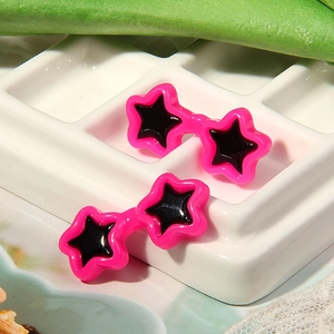 Detailed view of pink star-shaped doll glasses earrings on white display tray