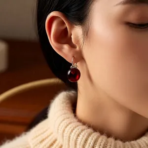 Elegant C-shaped earrings with Ancora red apple charms worn by a model in soft light