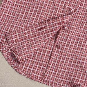 Detail of red and white plaid shirt showing fabric covered buttons and curved hemline
