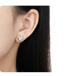 Close-up of model wearing heart-shaped silver earrings with irregular texture details