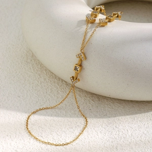 Detail of 18K gold-plated arrow hand chain with sparkling crystals on white ceramics