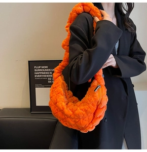 Close-up of orange quilted cloud shoulder bag texture with soft pleated velvet fabric