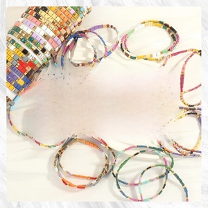 Macro shot of colorful Tila bead stretch bracelets with gold spacers on stone background