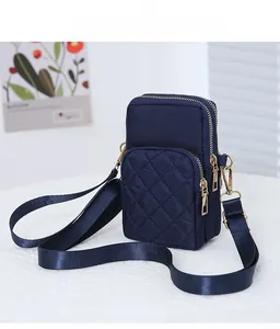 Detail view of a navy blue quilted crossbody bag with two gold-tone zipper compartments