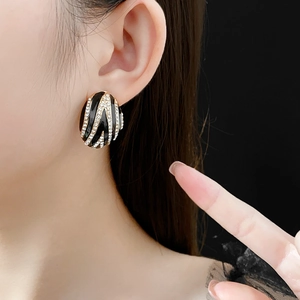 Close-up of model wearing black and gold oval earrings with sparkling striped pattern