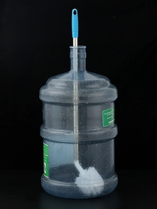 Detail of long-handled steel bucket brush with curved head cleaning a water jug