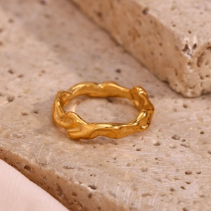 Detailed close-up of a gold-plated irregular wave ring on a light beige travertine stone