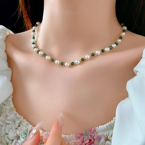 Detail shot of a vintage pearl and emerald-green beaded necklace on a model
