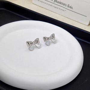Elegant silver bow knot stud earrings displayed on a white ceramic plate for a minimalist look