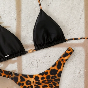 Detail of golden sun buckle on black bikini top with leopard print bottom textures