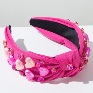 Detalle de la diadema rosa con nudo, pedrería brillante y dijes de corazón perlados