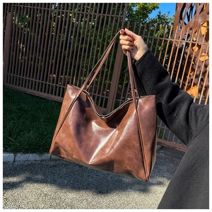 Brown leather tote bag held outdoors showing large capacity and soft texture