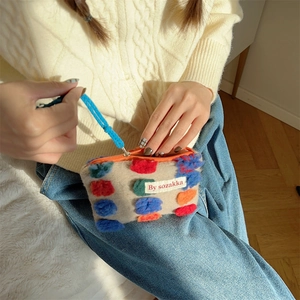 Detail of beige plush pouch with multi-color pom-poms and orange zipper closure