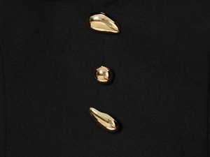 Detail view of liquid-shaped gold metal buttons on premium black elegant fabric