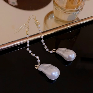 Macro view of long pearl drop earrings with gold metal chains and baroque pearls on black