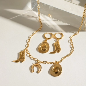 Parure de bijoux en acier doré avec pendentifs chapeau et botte de cow-boy sur fond blanc