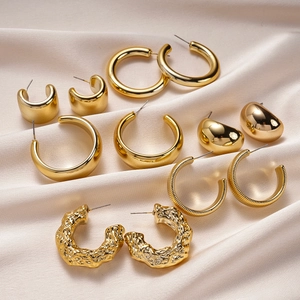 Macro shot of a 12-piece golden geometric earring set on champagne silk fabric background