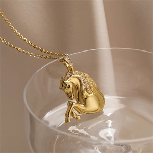 Détail d'un pendentif cheval doré avec cristaux posé sur le bord d'un verre