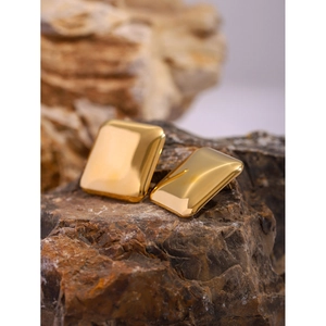Macro view of gold 18k stainless steel square earrings placed on a brown rock base