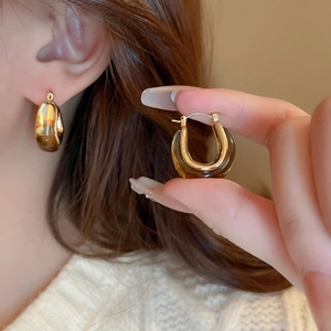 U-shaped gold earrings with amber resin detail shown in a stylish close-up shot