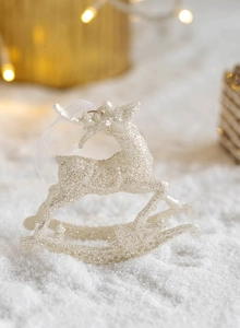 Macro shot of silver glitter reindeer ornament on snowy background with warm bokeh