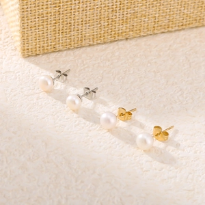 Minimalist pearl stud earrings set in gold and silver finishes on a textured background