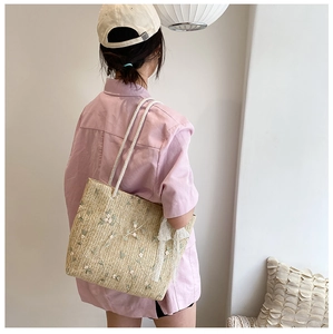 Detail of straw woven tote bag featuring delicate floral embroidery and white lace ribbon