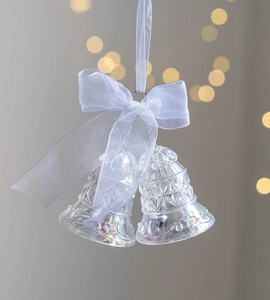 Close-up of transparent acrylic Christmas bells with white ribbons and festive bokeh lighting