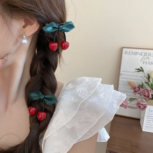 Close-up of a green satin bow hair clip with red cherry pendants worn by a model