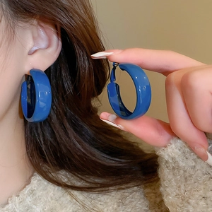 Close-up of glossy Klein blue C-shaped hoop earrings with high-shine lacquer finish