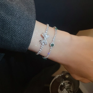Close-up of elegant bow bracelet and emerald green stone tennis chain on wrist