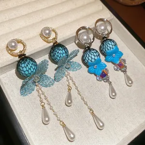 Elegant blue floral and mesh bow drop earrings with pearls and crystals on beige display