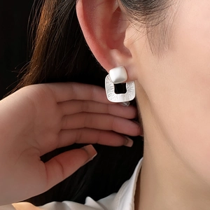 Close-up of matte silver square earrings with radial texture on a model's ear