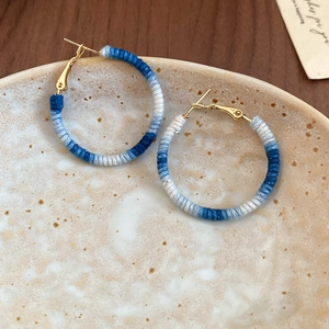 Dettaglio del filo di cotone blu e bianco avvolto intorno agli orecchini a cerchio
