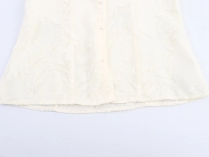 Detail of light yellow jacquard fabric with leaf patterns and elegant pearl buttons