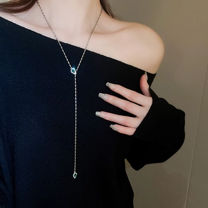 Silver Y-shape snake necklace with green teardrop pendants worn on a black top