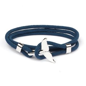 Close-up of deep blue woven rope bracelet with silver whale tail pendant on white background