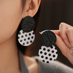 Detail of retro black and white polka dot acrylic earrings worn on a model's ear