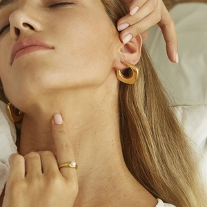 Detail view of model wearing thick gold hoop earrings and a gold pearl ring in soft light