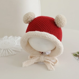 Detail einer roten Strickmütze für Babys mit zwei Plüschpompons und Ohrenklappen