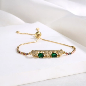 Detail of adjustable gold heart bracelet with green gemstones and rainbow accents