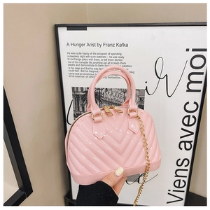 Close-up of pink jelly shell bag with gold chain strap held by hand against minimalist poster