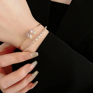 Detailed view of layered gold bangle featuring a pink zircon butterfly on a model wrist